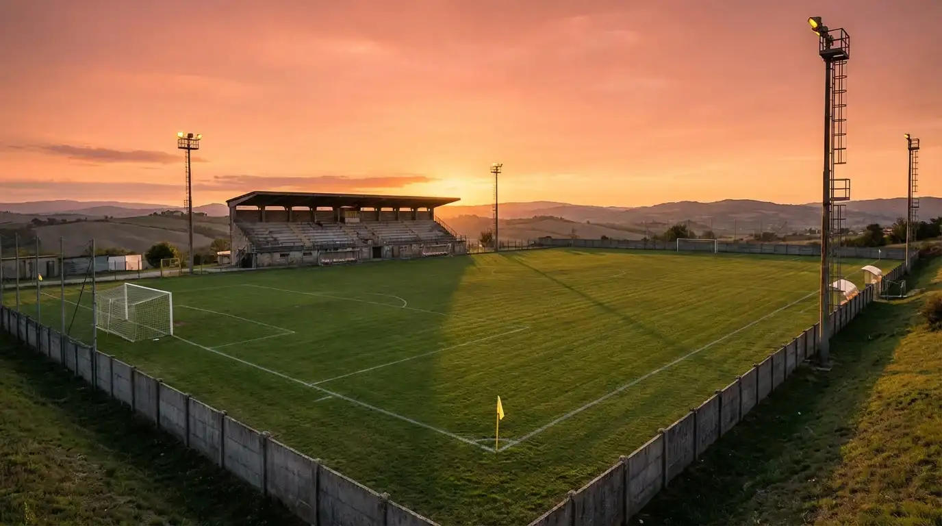 Stadio di calcio di provincia con tribuna coperta e campo in erba naturale al tramonto